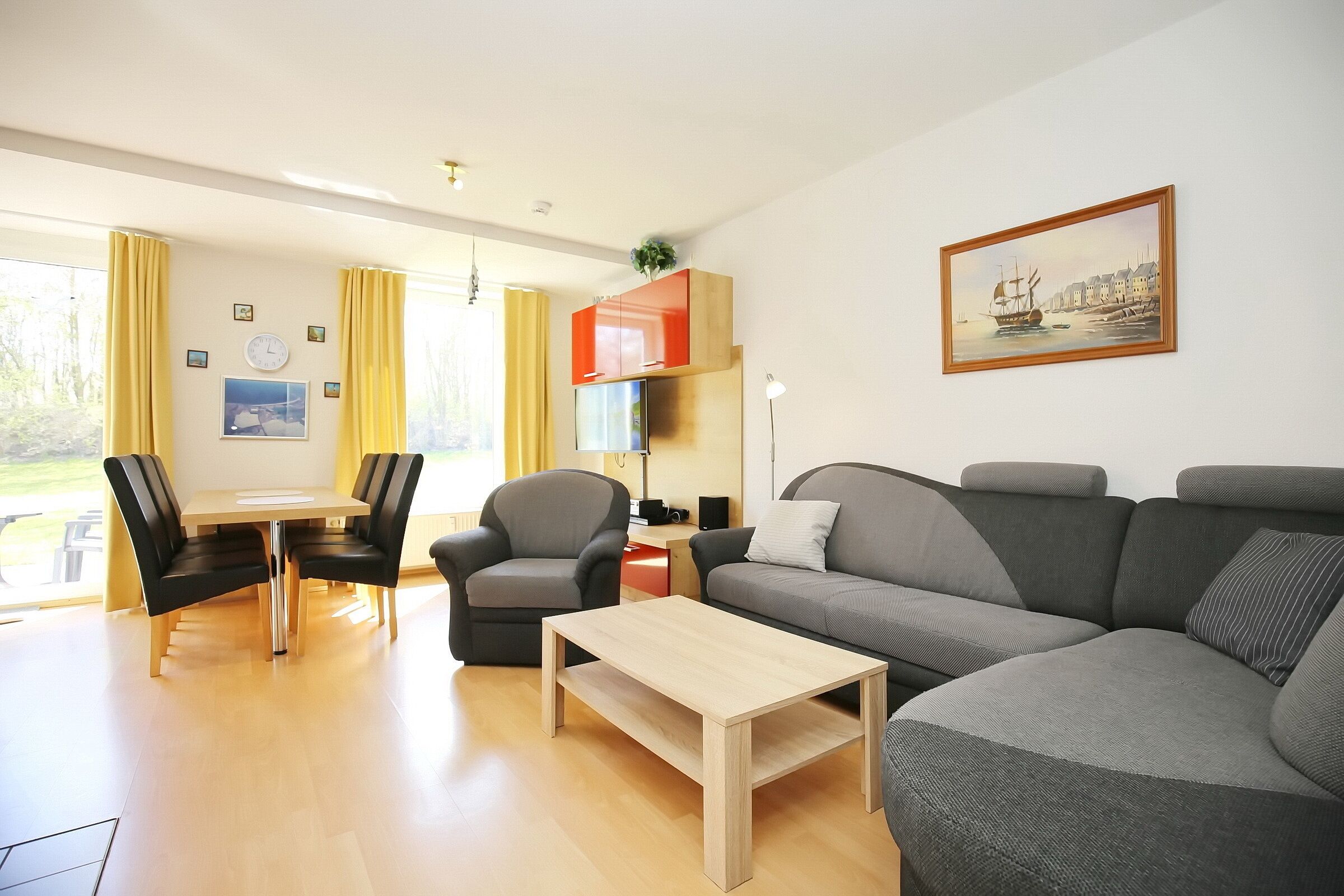 Een moderne woonkamer met een grijze bank, een houten salontafel en een eethoek met een tafel en stoelen.