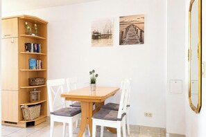 A room with a wooden table, white chairs, a bookshelf, and two wall-mounted pictures. - Waterkant - Bernstein Wohnung 13 (Ostseebad Boltenhagen)