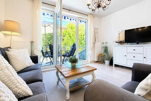 En moderne stue med sofa, sofabord, fjernsyn og udsigt til det fri gennem store glasdøre.