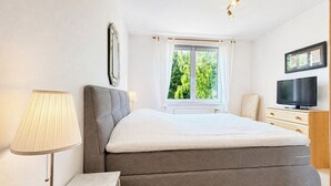 Una camera da letto con un letto, una televisione, una finestra con tende e una lampada.