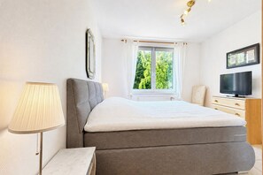 A bedroom with a bed, a TV, a window with curtains, and a lamp. - Waterkant - Bernstein Wohnung 13 (Ostseebad Boltenhagen)
