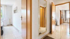 Un corridoio d'albergo con un grande specchio, porte in legno e pavimento piastrellato.