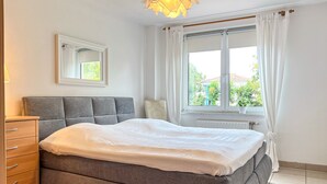 A bedroom with a bed, a dresser, a window with curtains, and a ceiling light fixture.