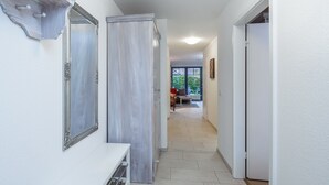 A hallway with a white wall, a mirror, a white console table, and a door leading to a room. - Papillon Wohnung 05-2 (Ostseebad Boltenhagen)