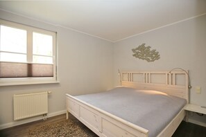 A bedroom with a single bed, a radiator, a window with blinds, and a wall-mounted light fixture. - Papillon Wohnung 05-4 (Ostseebad Boltenhagen)
