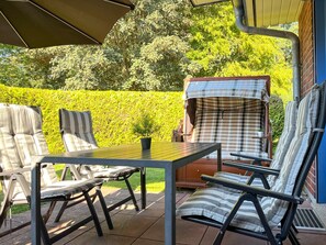 An outdoor patio with a table and chairs, a covered grill, and a hedge in the background. - Papillon Wohnung 05-4 (Ostseebad Boltenhagen)