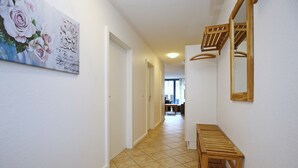 Un pasillo con suelo de baldosas, un banco de madera, un cuadro de flores y un espejo en la pared.