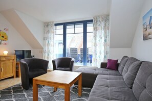 Un salon comprenant un canapé, deux fauteuils, une table basse en bois et un téléviseur posé sur un meuble en bois.