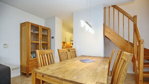 Un comedor con una mesa y sillas de madera, un armario de madera con puertas de cristal, y una escalera con barandilla de madera.