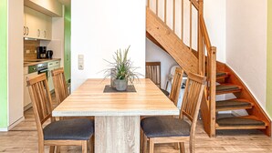 A dining area with a wooden table and chairs, a potted plant, and a wooden staircase.