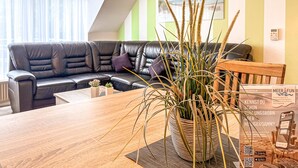 A modern living room with a leather sofa, a wooden dining table, and a potted plant.