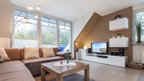 Un salon moderne avec un canapé d’angle, une table basse en bois, un téléviseur à écran plat et un meuble de rangement blanc.