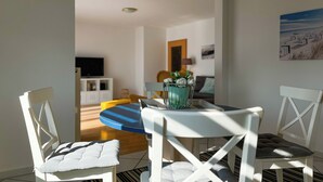 A dining area with a round table, white chairs, and a blue chair. There is a vase with flowers on the table. - Waterkant - Muschel Wohnung 1 (Ostseebad Boltenhagen)