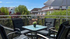A balcony with a glass table, two chairs, and a potted plant. - Waterkant - Muschel Wohnung 1 (Ostseebad Boltenhagen)
