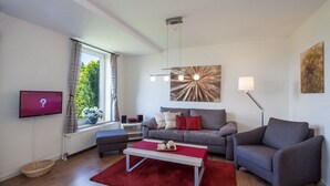 Ett modernt vardagsrum med en grå soffa, en röd matta, en platt-TV och en stor, abstrakt tavla.