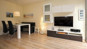 A modern living room with a flat-screen TV, white cabinets, a dining table with chairs, and a small side table.