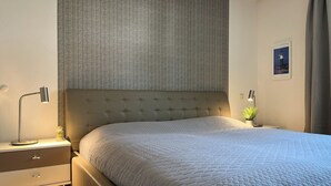 A neatly made bed with a quilted cover, a bedside lamp, and a small potted plant on the nightstand.