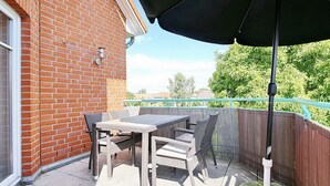 Eine Terrasse mit Tisch und Stühlen, einem schwarzen Sonnenschirm und einem Holzzaun.