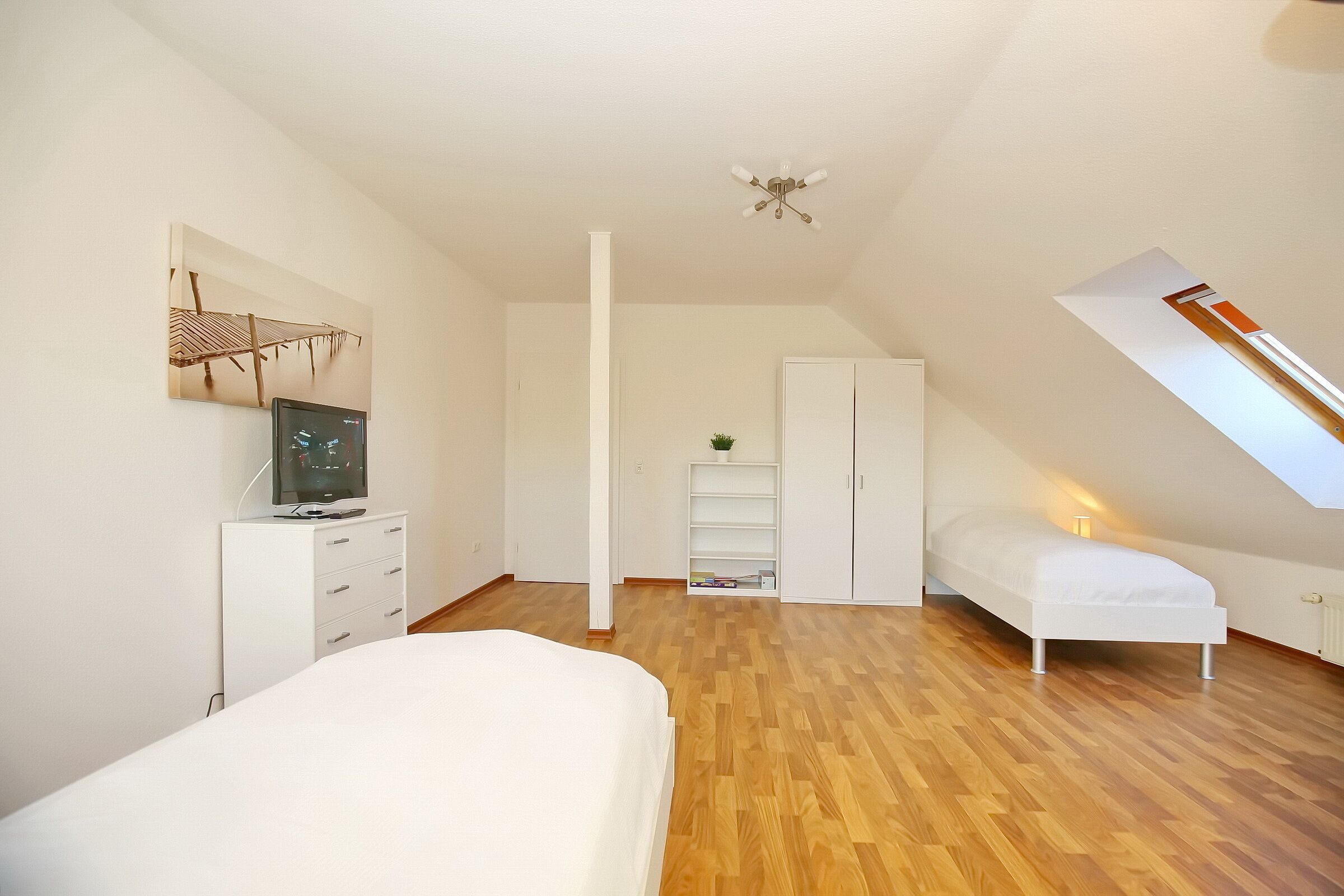 Een slaapkamer met een bed, een televisie op een dressoir, een kledingkast en een dakraam.