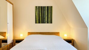 Ein ordentlich bezogenes Bett in einem Zimmer mit einem Holzkopfteil, zwei Nachttischen mit Lampen und einer an der Wand befestigten Bambus-Kunstartikel.