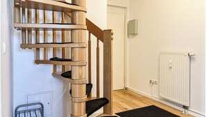 Eine Holzspirale mit schwarzen, gepolsterten Stufen, einem Heizkörper und einer schwarzen Matte auf Holzdielen.