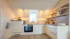 A modern kitchen with a built-in oven, white cabinetry, and wooden flooring. - Haffblick Wohnung 50 (Ostseebad Boltenhagen)