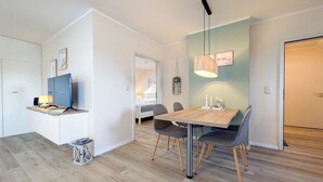 A modern kitchen with a wooden table and chairs, a built-in stove, and a hanging pendant light. - Haffblick Wohnung 50 (Ostseebad Boltenhagen)