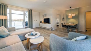 A modern living room with a sofa, a dining table, and a TV. - Haffblick Wohnung 50 (Ostseebad Boltenhagen)