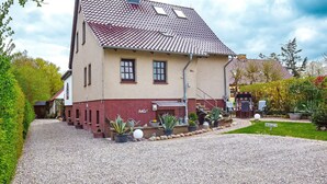 A two-story house with a tiled roof, a gravel driveway, and potted plants in the front yard. - Einliegerwohnung Arielle 1 (Boltenhagen/Redewisch)