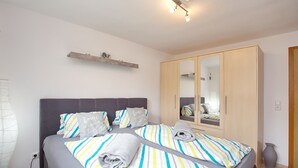 A neatly made bed with striped bedding, a bedside table, a wardrobe, and a shelf above the bed. - Einliegerwohnung Arielle 1 (Boltenhagen/Redewisch)