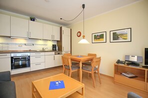 Una cocina moderna con armarios blancos, horno empotrado y comedor con sillas y mesa de madera.