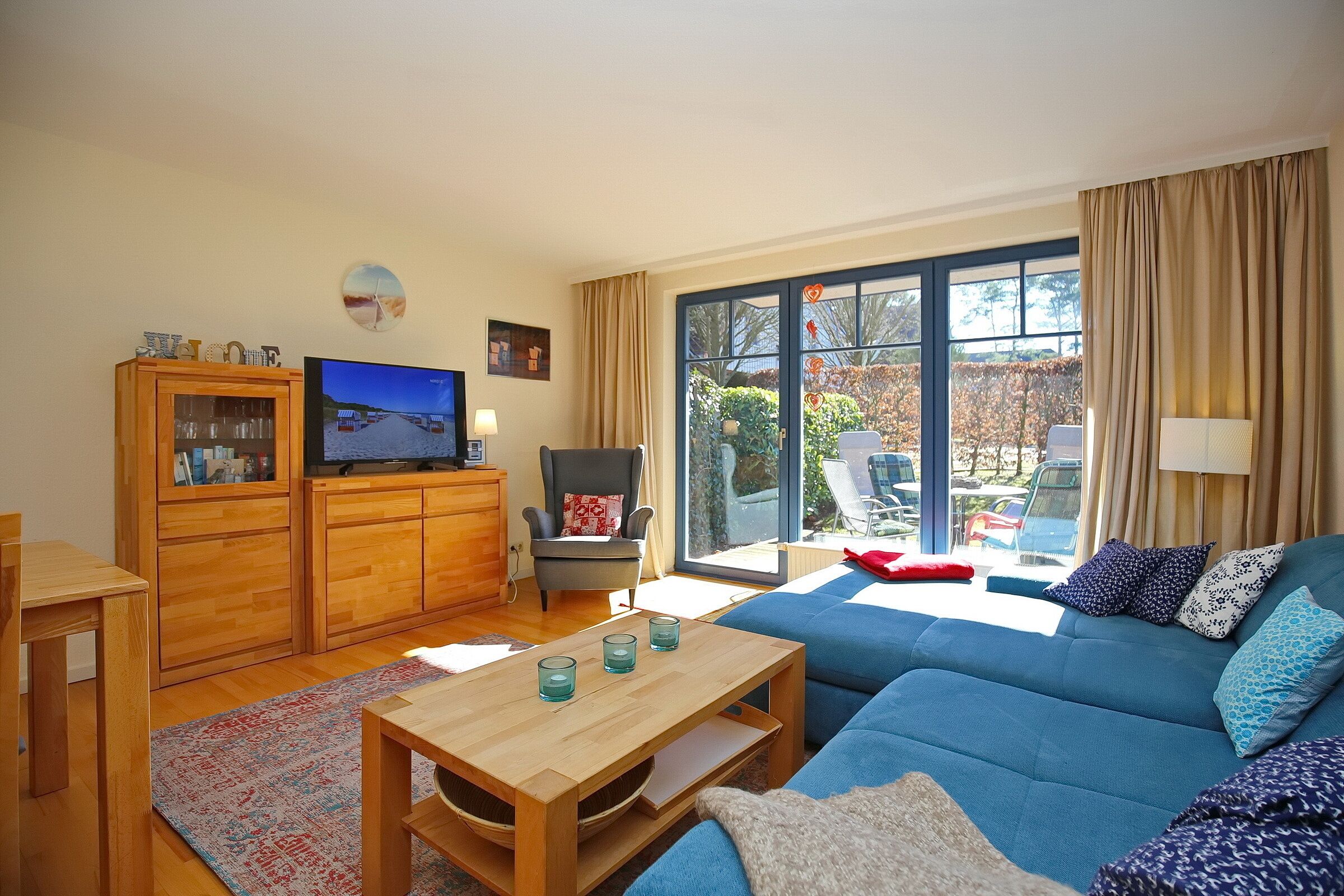 A living room with a blue sofa, wooden cabinets, a television, and a large window with curtains.