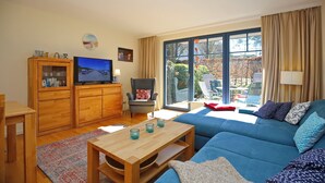 Uma sala de estar com um sofá azul, armários de madeira, uma televisão e uma janela grande com cortinas.