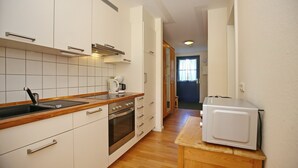 Cozinha com armários brancos, forno de aço inoxidável, micro-ondas e bancada de madeira.
