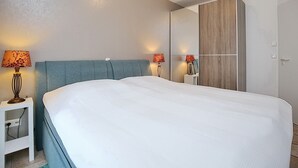 Quarto moderno com uma cama grande, duas mesas de cabeceira com luminárias e um guarda-roupa.