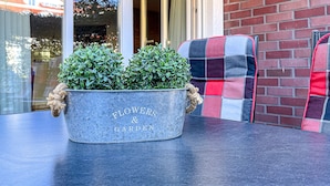 Um vaso de metal com a inscrição 'Flowers & Garden', colocado sobre uma mesa.