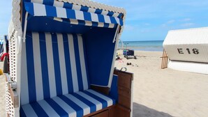 Ein Liegestuhl mit einem blau-weiß gestreiften Sonnendach, eine Holzbank und im Hintergrund eine weiße Struktur mit der Aufschrift "E18".