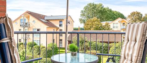 A balcony with a round glass table, two striped chairs, and a purple umbrella.