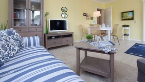 Ein Wohnzimmer mit einer Couch, einem Fernseher, einem Schrank und einem Essbereich mit Stühlen und einem Tisch.