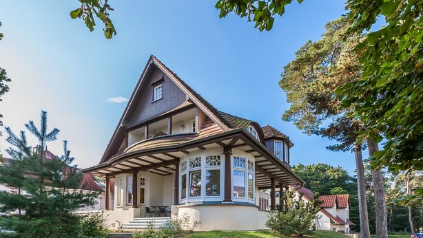 Une maison à deux étages, dotée d’un toit à pignon, d’un porche couvert et d’un petit jardin devant.