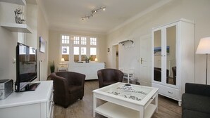 Un salon moderne doté d’un téléviseur à écran plat, de deux fauteuils en cuir marron, d’une table basse blanche et d’une grande armoire blanche avec un miroir.