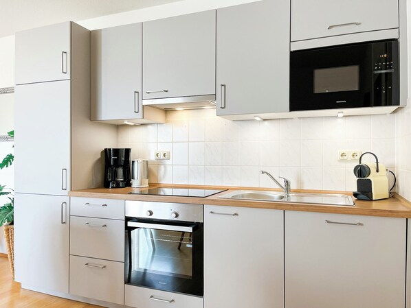 Een moderne keuken met witte kasten, een inbouwoven, een magnetron en een koffiezetapparaat op het aanrecht.