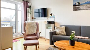Ein modernes Wohnzimmer mit einem grauen Sofa, einem rosa Sessel, einem Holztisch und einem an der Wand montierten Fernseher.