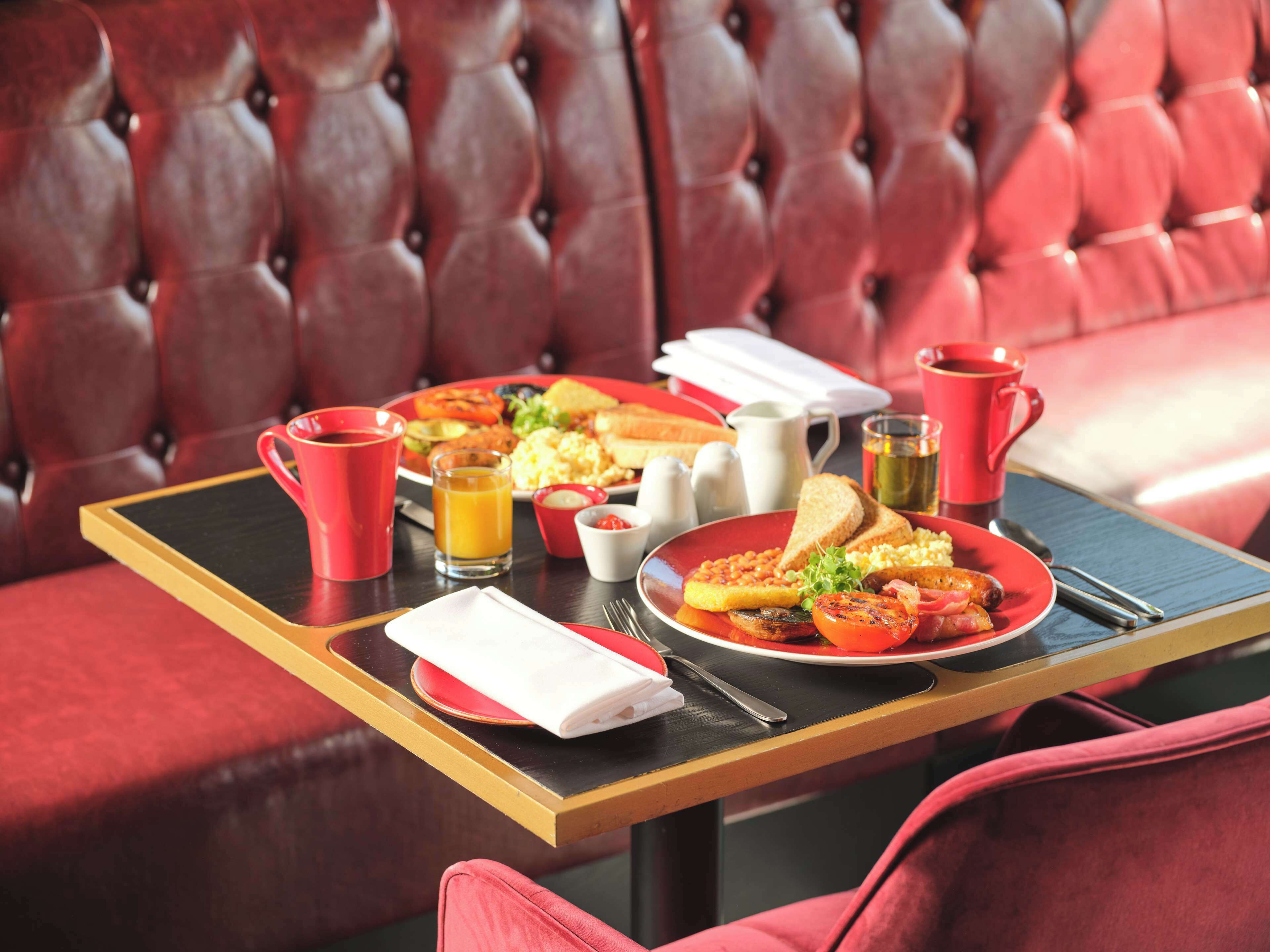 A dining table with breakfast items, a red cup, a glass of orange juice, and a red pitcher.