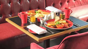 A dining table with breakfast items, a red cup, a glass of orange juice, and a red pitcher.