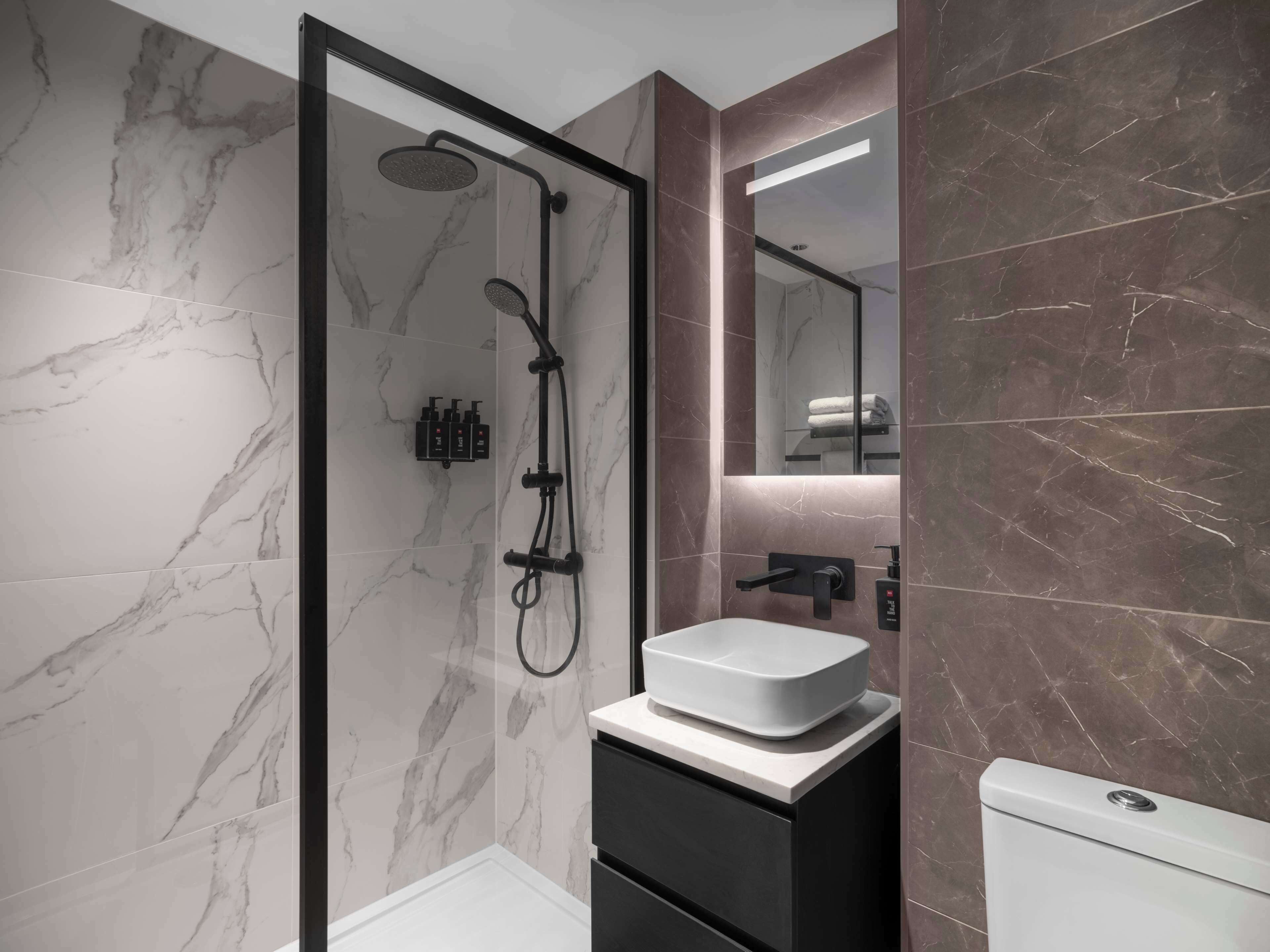 Un baño moderno con ducha envuelta en vidrio, un lavamanos blanco y un mueble oscuro.