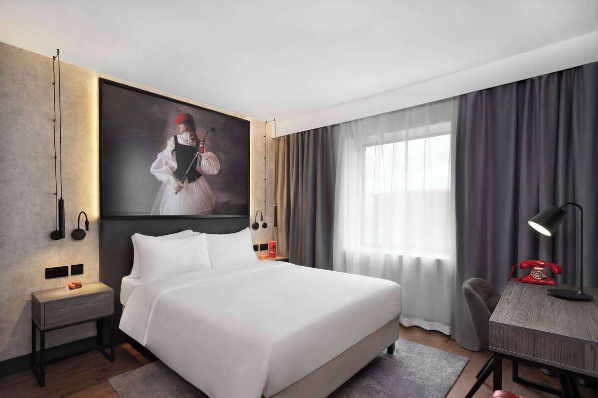 A modern hotel room with a large bed, bedside tables, a desk, and a chair.