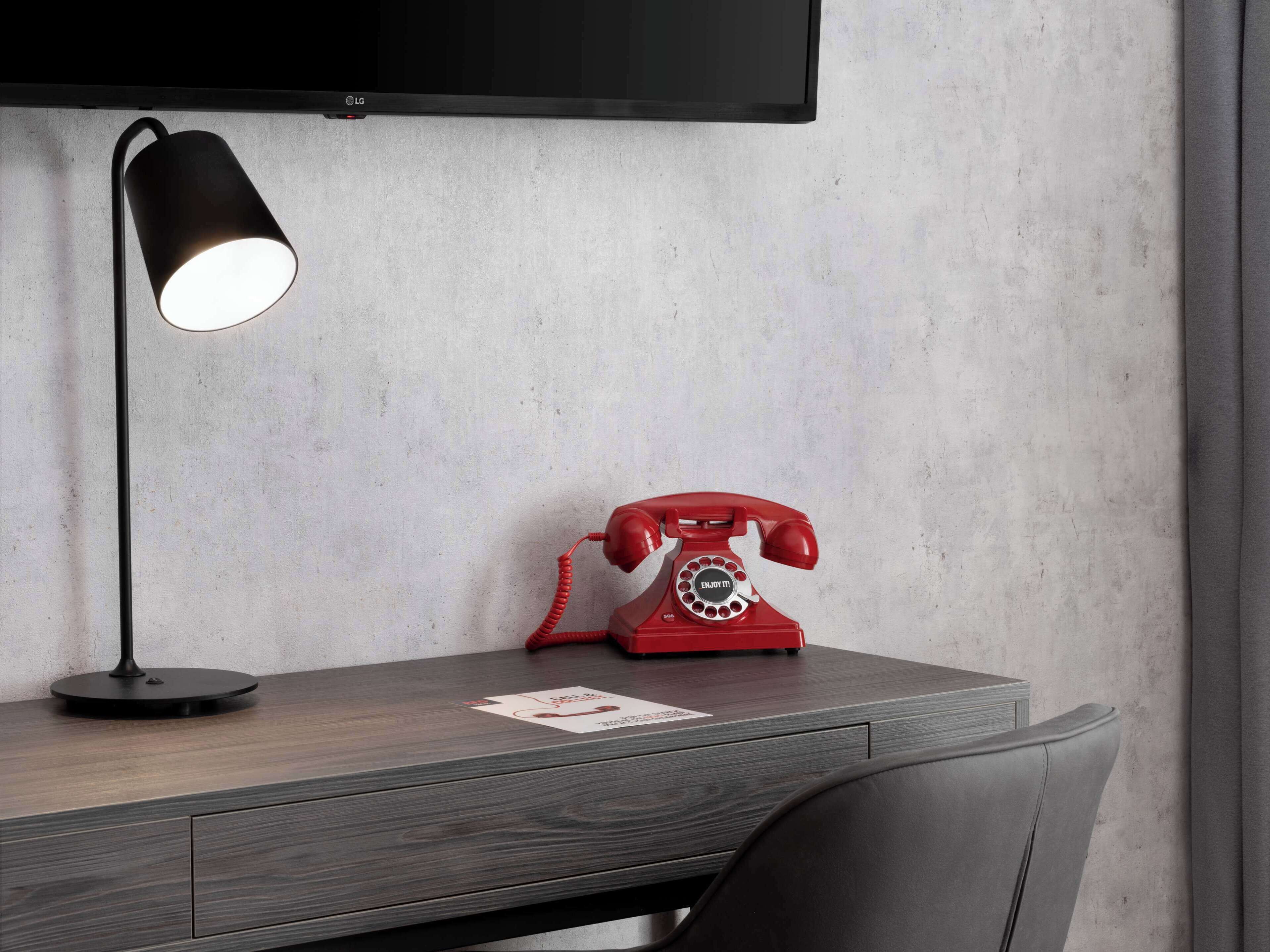 A desk with a red rotary phone and a black desk lamp.