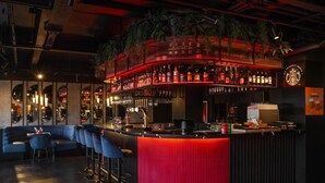 A bar area with a curved counter, bar stools, and a red accent wall. - Radisson RED London Gatwick Airport (Crawley)