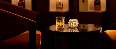 A bar area with shelves displaying bottles, a round table with a glass and a decorative item, and a red chair.